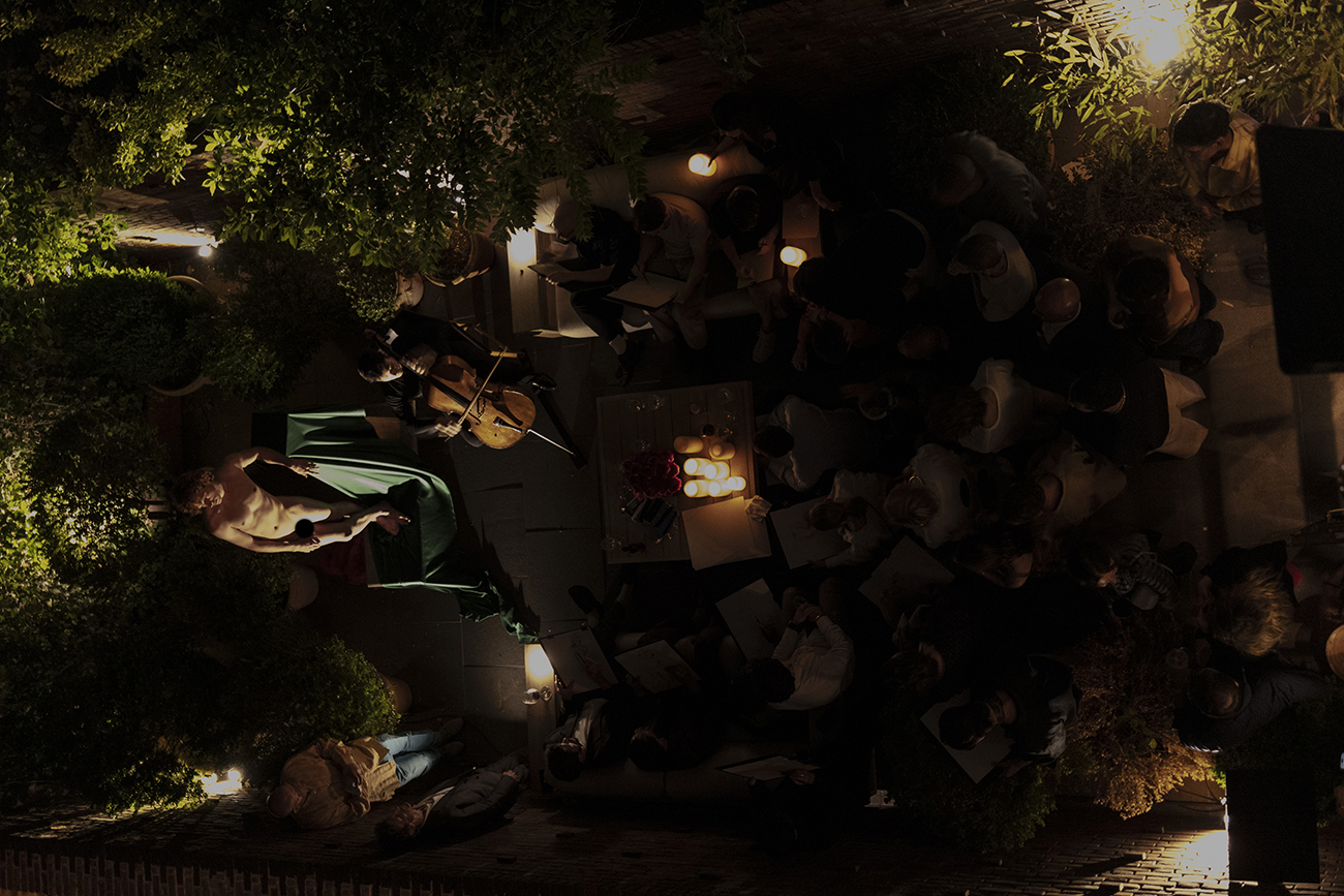Overhead view of a candlelit salon gathering with a cellist performing